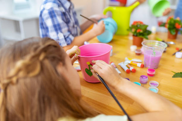 Girl painting. Close up of dark-haired girl painting with gouache on pink bucket for plant